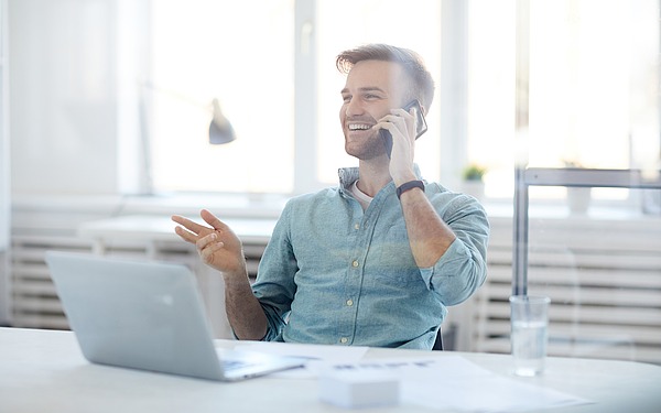 Mann sieht an Laptop und telefoniert im Büro.