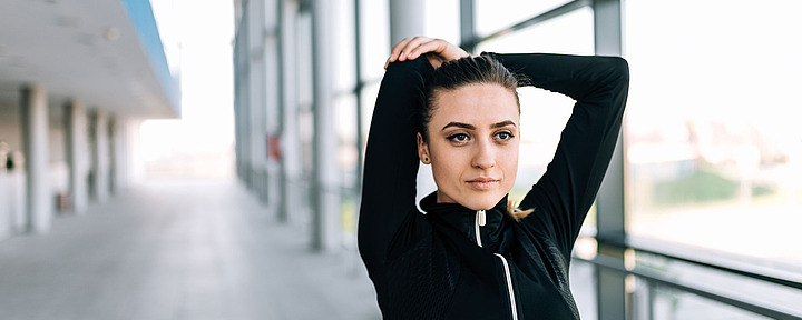 Junge Frau macht Dehnübung. Sie hält ihre Arme über dem Kopf.